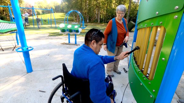 Person in plays a playground xylophone while sitting in a wheelchair.